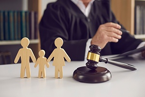 wooden figurines of a family with a judge gavel on the side and a judge in the background