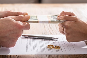 a couple pulling on a stack of money with divorce papers and rings on a desk