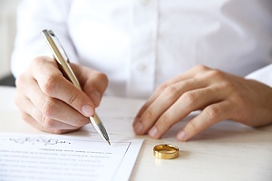 a women signing a divorce agreement with her wedding ring in front of her