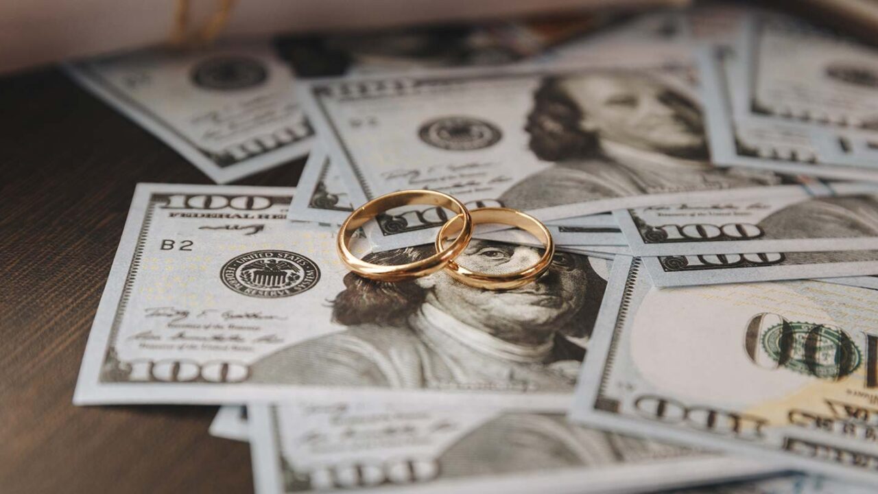 gold wedding rings on top of one hundred dollar bills