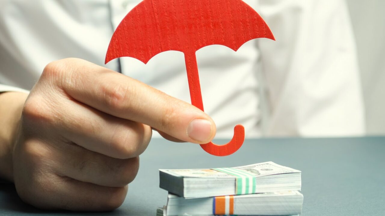insurance agent holds a red umbrella over dollar bills