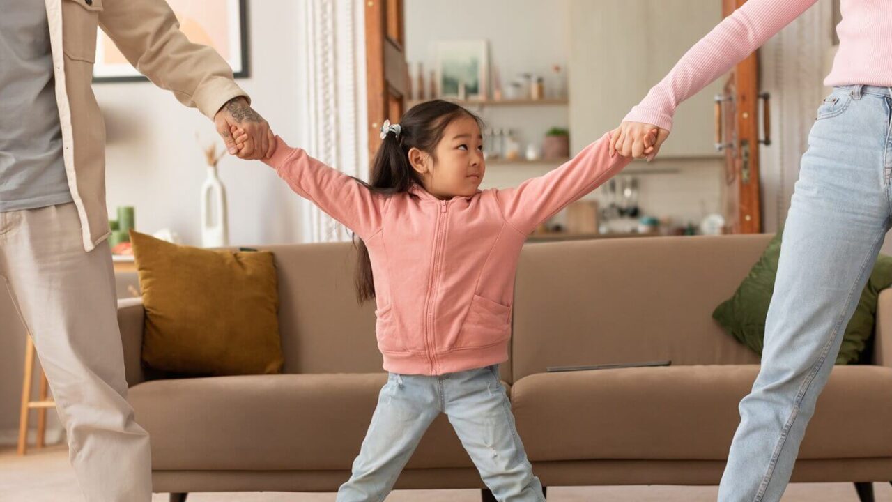 asian parents pulling daughter's hands in different directions standing indoor
