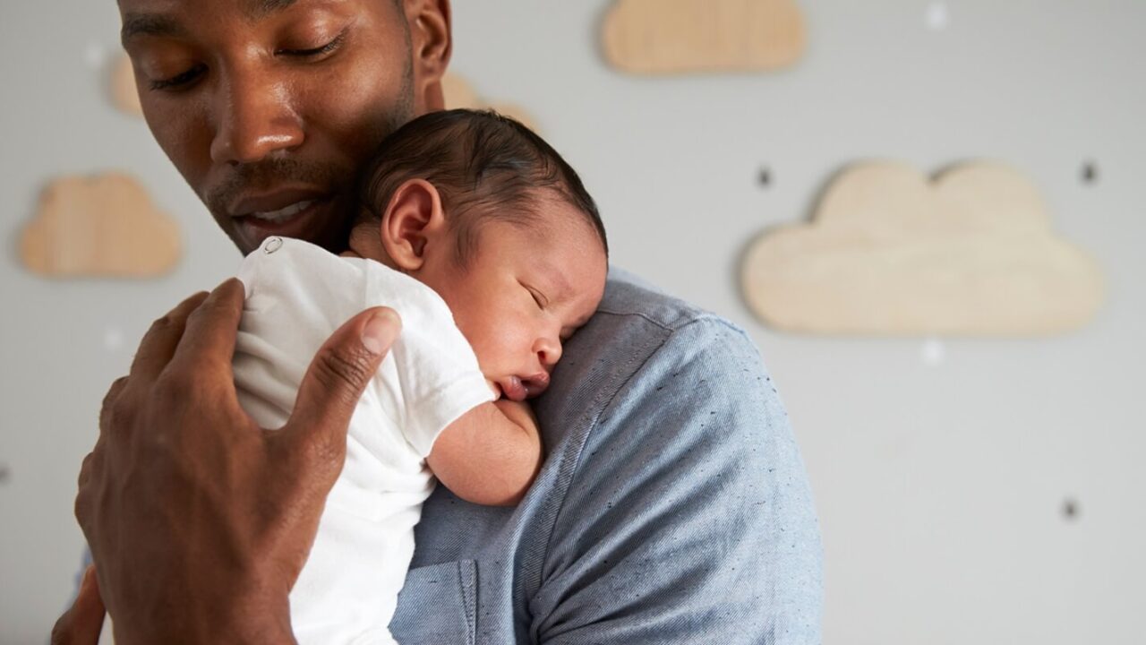 father holding newborn baby son In nursery