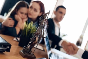 bronze statue of Themis stands on table, behind which sits divorcing parents with little girl